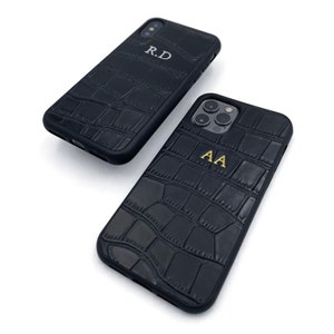 May include: Two black phone cases with a crocodile-embossed leather texture. One case has the initials "R.D." and the other has the initials "A.A."