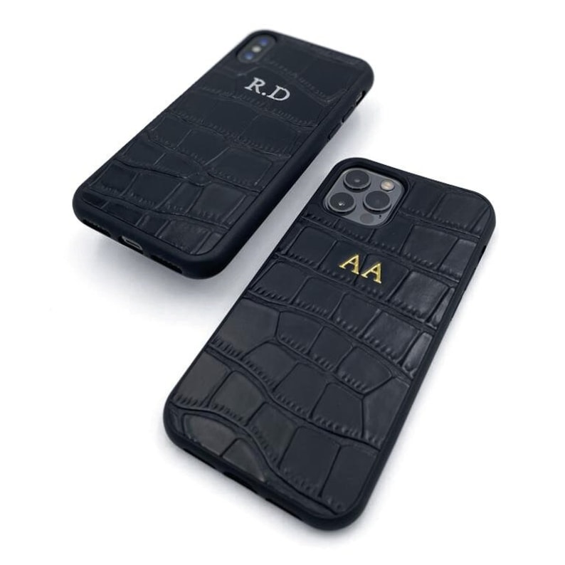 May include: Two black phone cases with a crocodile-embossed leather texture. One case has the initials "R.D." and the other has the initials "A.A."