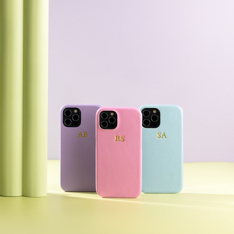 May include: Three phone cases in different colors: lavender, pink, and light blue. Each case has a different set of initials on the back: AB, RS, and SA.