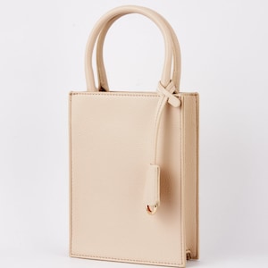 May include: A beige leather tote bag with a top handle and a knotted strap. The bag has a rectangular shape and a smooth, textured finish.