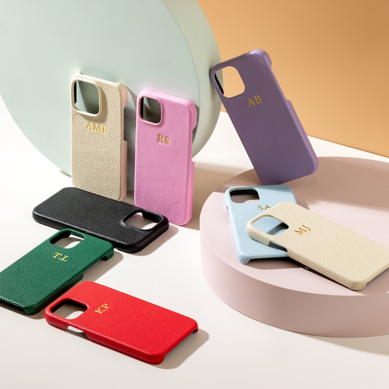 May include: Assortment of eight personalized phone cases in various colors and materials. The cases feature different initials, including "AB", "RS", "AME", "TL", "KP", "SA", and "MIJ".