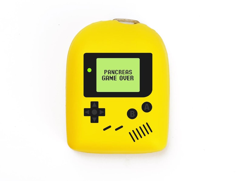 May include: A yellow, handheld game console-shaped device with a black screen displaying "PANCREAS GAME OVER" in green text. The device has black buttons and a directional pad, resembling a classic video game console.