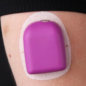 May include: A purple medical device attached to a person's arm with a white adhesive patch.