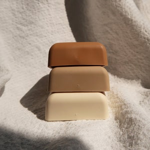 May include: Three square-shaped containers stacked on top of each other. The top container is brown, the middle container is beige, and the bottom container is white.