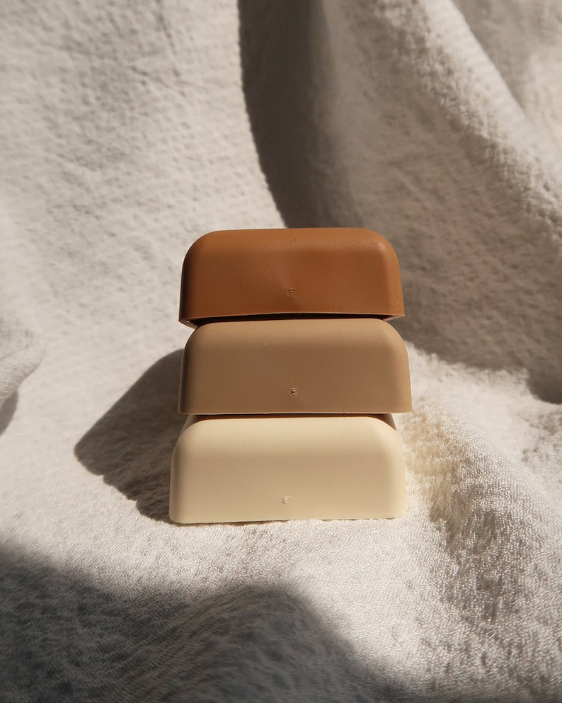 May include: Three square-shaped containers stacked on top of each other. The top container is brown, the middle container is beige, and the bottom container is white.