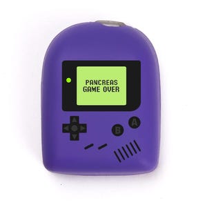 May include: A purple novelty item in the shape of a retro handheld game console. The screen displays "PANCREAS GAME OVER" in white text on a green background. It has black control buttons and a small green light.