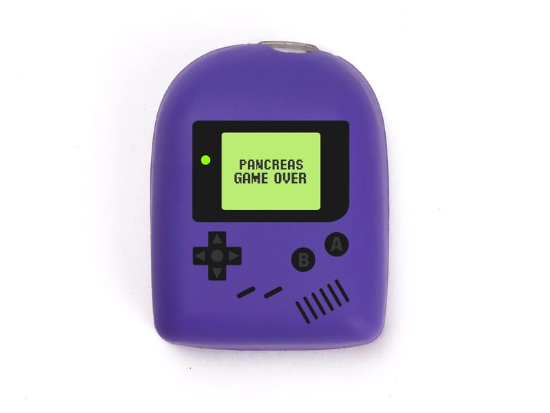 May include: A purple novelty item in the shape of a retro handheld game console. The screen displays "PANCREAS GAME OVER" in white text on a green background. It has black control buttons and a small green light.