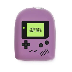 May include: A lavender-coloured novelty item shaped like a retro handheld game console. The screen displays "PANCREAS GAME OVER" in white text on a green background. Black buttons and directional pad are also visible.