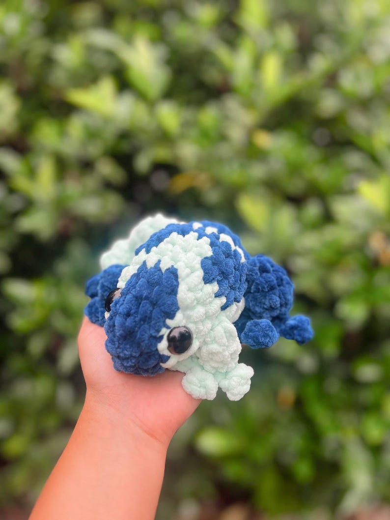 May include: A crocheted frog toy with blue and light green yarn. The frog has black eyes and a textured surface.