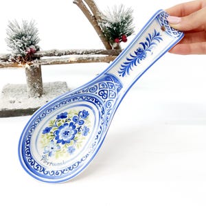 Puede incluir: Un reposacucharas de cerámica azul y blanco con un diseño floral. El reposacucharas tiene un mango largo y un cuenco ovalado. La palabra "Portugal" está escrita en el reposacucharas.