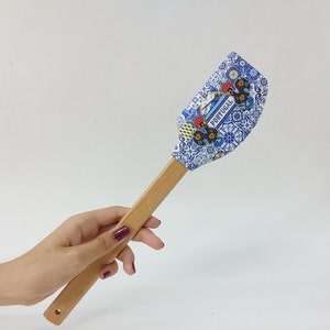 May include: A blue and white spatula with a wooden handle. The spatula features a Portuguese design with a rooster and the word "Portugal" on it.