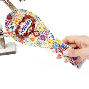 Könnte beinhalten: Ein dekorativer Löffelhalter mit einem farbenfrohen, gemusterten Design. Der Löffelhalter zeigt ein Mosaik aus blauen, gelben, roten und weißen Fliesen. Das Wort "PORTUGAL" ist in einem dekorativen Rahmen dargestellt.