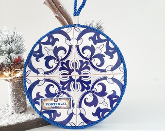 May include: Blue and white ceramic trivet with a Portuguese tile pattern and a blue rope handle. The trivet has the word "PORTUGAL" printed on it.