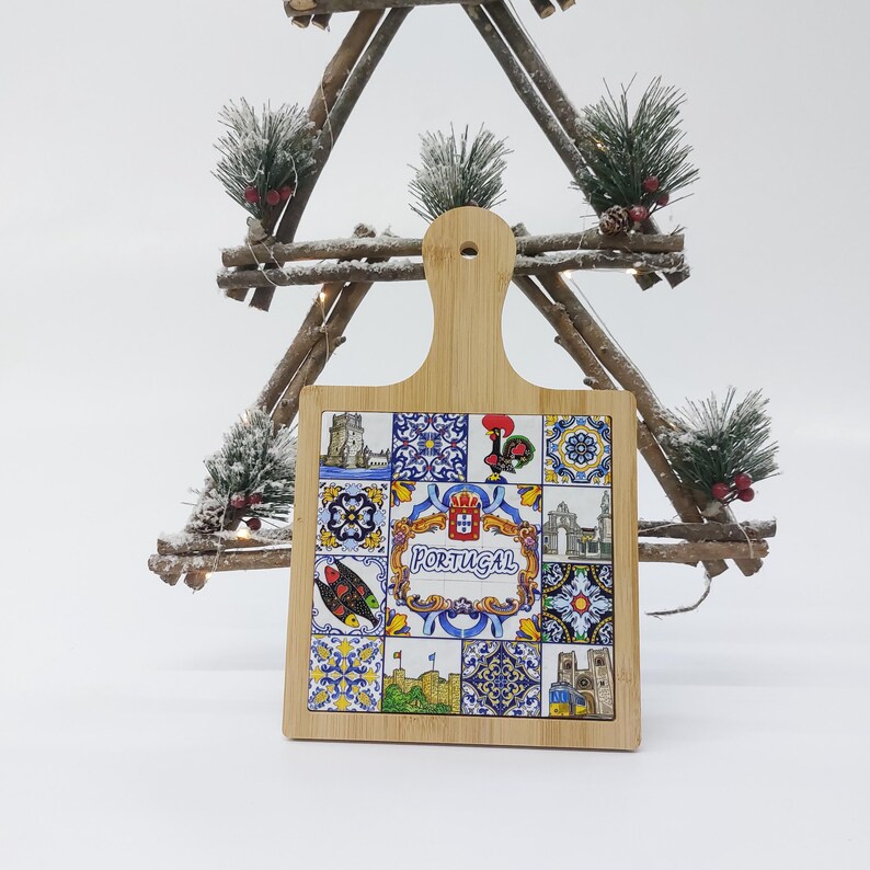 May include: A wooden cutting board with a handle, featuring a colorful design of Portuguese tiles and the word "PORTUGAL".