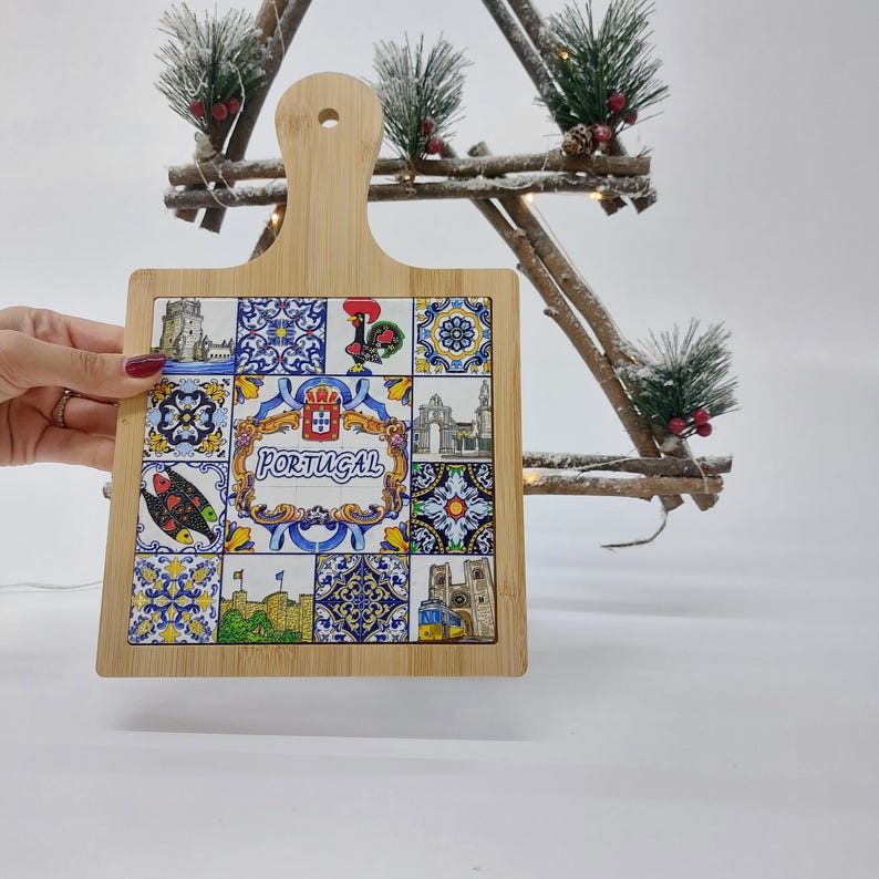May include: A square wooden cutting board with a handle. The board is decorated with a colorful tile design featuring Portuguese motifs, including a rooster, a coat of arms, and the word "PORTUGAL".