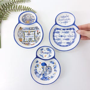 Puede incluir: Tres fuentes de cerámica blanca con bordes azules y diseños decorativos. Cada fuente tiene una sección superior pequeña y una sección inferior más grande. Los diseños incluyen peces, un gallo y patrones de azulejos portugueses. La palabra "Portugal" está impresa en cada fuente.