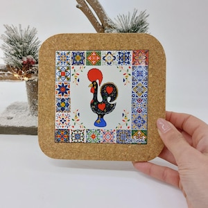 May include: Cork coaster featuring a colourful rooster design with a border of Portuguese tiles. The rooster is black with red accents and a blue base. The text "PORTUGAL" is printed in the bottom right corner.