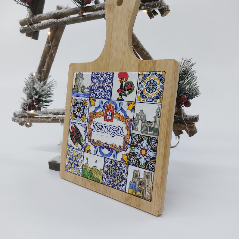 May include: A square wooden cutting board with a handle. The board has a colorful tile design with images of Portuguese landmarks and the word "PORTUGAL" in the center.
