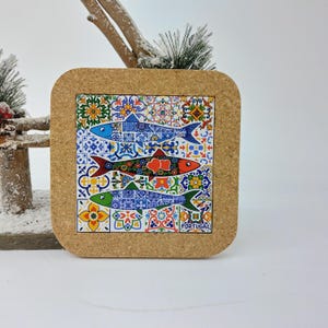 Puede incluir: Un posavasos de corcho con un diseño colorido que presenta tres peces y un patrón de azulejos. El posavasos tiene la palabra "PORTUGAL" impresa.