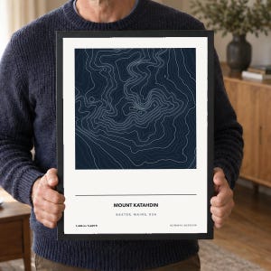 May include: A framed topographic map print of Mount Katahdin in Baxter, Maine, USA. The artwork features white contour lines on a dark blue background, with the text Mount Katahdin, Baxter, Maine, USA, 1,606 m / 5,269 ft, and 45.9044°N / 68.9214°W.
