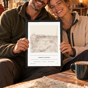 Peut inclure: Une impression cartographique encadrée intitulée Camino de Santiago, présentant une ligne d'itinéraire topographique rouge sur fond crème. Le texte indique Camino Frances, Saint-Jean-Pied-de-Port to Santiago, Maria & Luke, 34 days, Buen Camino, 775 km.