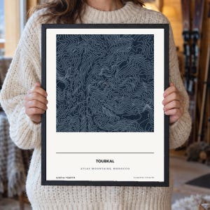 May include: A framed topographic map print of Toubkal in the Atlas Mountains, Morocco. The artwork features white contour lines on a dark blue background, with the text TOUBKAL, ATLAS MOUNTAINS, MOROCCO, 4,167 m / 13,671 ft, and coordinates.