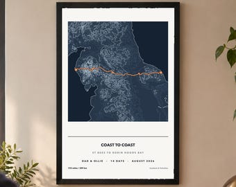 May include: A framed wall print featuring a dark blue topographic map with a bright orange route line. Text reads: COAST TO COAST, ST BEES TO ROBIN HOOD'S BAY, DAD & OLLIE, 14 DAYS, AUGUST 2026, 192 miles / 309 km, and Cumbria & Yorkshire.