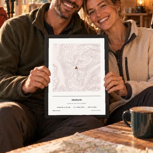 May include: A framed topographic map print of Helvellyn featuring contour lines in a light pink hue on a white background. The print includes a small brown triangle icon, the text Helvellyn, Sunrise on the summit, 21 June 2026, 950m / 3,117ft.