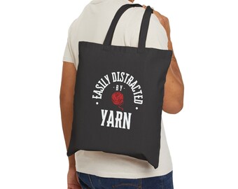 May include: A black tote bag with white text that reads "Easily Distracted by Yarn" with a red yarn ball graphic.