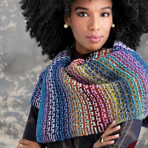 May include: A woman wearing a colourful knitted shawl with a geometric pattern. The shawl is made with a variety of shades of blue, purple, orange, and green yarn.