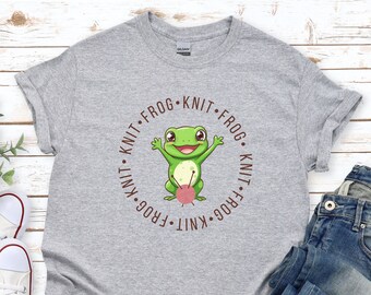 May include: Gray t-shirt with a green frog holding a ball of yarn. The frog is surrounded by the text "Knit Frog Knit Frog Knit Frog Knit".