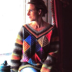 May include: A colorful, geometric-patterned sweater with a V-neck. The sweater features a patchwork design with various colors including blue, orange, red, and yellow. The sleeves and body have striped patterns. The person is wearing blue jeans.