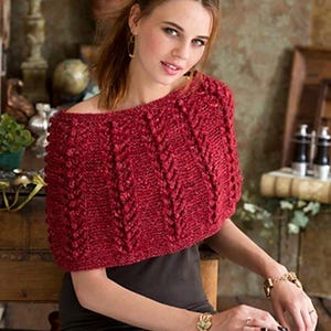 May include: A red knitted shawl with a textured cable design. The shawl is worn over the shoulders and has a wide, off-the-shoulder neckline. The color is a deep, rich red, and the knit pattern creates a visually interesting texture. The shawl is a cozy and stylish accessory.