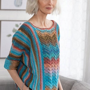 Könnte beinhalten: Ein gehäkeltes Oberteil mit einem gestreiften Muster in Blautönen, Braun und Rosa. Das Oberteil hat eine lockere Passform und einen runden Ausschnitt.