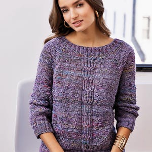 Könnte beinhalten: Ein lilafarbener Pullover mit Zopfmuster und einem gesprenkelten Muster. Der Pullover hat einen runden Ausschnitt und lange Ärmel.