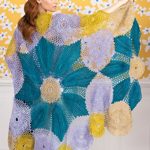 Op de afbeelding: Een gehaakte sjaal met een bloemenpatroon in tinten turquoise, lavendel en geel. De sjaal is gemaakt van verschillende ronde motieven die aan elkaar zijn verbonden.