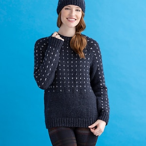 May include: A navy blue sweater with a white heart pattern. The sweater has a round neckline and long sleeves. The model is wearing black leggings with a plaid pattern.