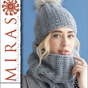 May include: A grey knitted hat with a white pom pom and a matching grey knitted neck warmer. Both the hat and neck warmer are made with a textured stitch pattern. The model is wearing the hat and neck warmer and has blonde hair and blue eyes. The image is from the 10th Anniversary Collection of the Mirasi brand. The text "Ushya M5271" is also visible in the image.