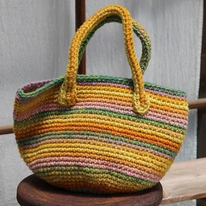 May include: A crocheted tote bag with a striped pattern in shades of yellow, green, pink, and orange. The bag has two thick crocheted handles.