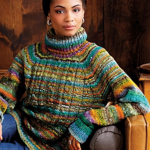 Puede incluir: Un jersey de cuello alto de manga larga multicolor con un patrón de punto texturizado. El jersey presenta una vibrante mezcla de colores que incluyen verde, azul, naranja y morado. La modelo lleva el jersey con unos vaqueros azules.