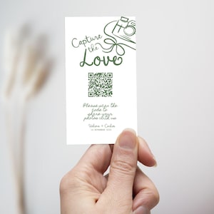 May include: A white card with green text and a QR code is held in a hand. The card reads "Capture the Love" with a camera illustration. Below the QR code is the text "Please scan the code to share your photos with us."