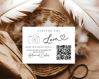 May include: White card with black text that says "Capture the Love" with a heart symbol. Below the text is a black and white illustration of a camera with a heart inside. Below the camera is a QR code and the text "Share your photos with us. Scan the code with your smartphone and upload your photos. Helena and Carlos."
