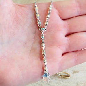 May include: Silver-toned necklace with iridescent crystal accents. The Y-shaped pendant features a series of small, round crystals and a larger, teardrop-shaped crystal at the bottom. The necklace is displayed against a neutral background.