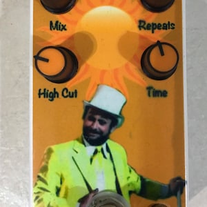 May include: A white pedal with a yellow and orange sun design. The pedal has four knobs labeled "Mix", "Repeats", "High Cut", and "Time". There is a foot switch in the center of the pedal.