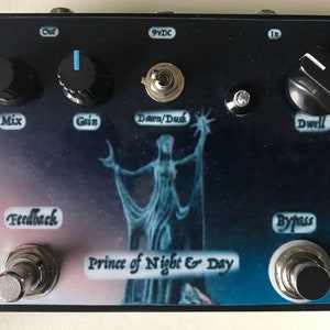 Può includere: Un pedale per effetti di chitarra nero con uno sfondo blu e viola che presenta un'immagine stilizzata di una donna con una stella. Il pedale ha manopole etichettate come "Mix", "Gain", "Dwell" e "Dawn/Dusk". Ha anche due interruttori a pedale etichettati come "Feedback" e "Bypass". Il testo "Prince of Night & Day" è stampato sul pedale.