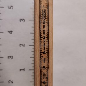 May include: A wooden ruler with black markings and the text "RIDGID No. 618 Plumbers' Rule." The ruler measures up to 6 inches. The numbers and markings are printed in black ink on the light brown wood.