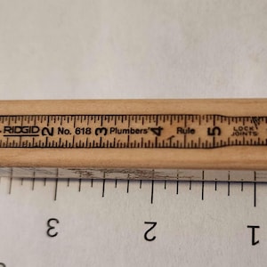 May include: A wooden Ridgid No. 618 Plumbers Rule with black markings. The ruler is marked with inch measurements from 1 to 6, and the text "LOCK JOINTS". The ruler is light brown in color.