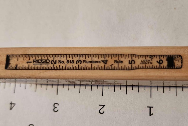 May include: A wooden Ridgid No. 618 Plumbers Rule with black markings. The ruler is marked with inch measurements from 1 to 6, and the text "LOCK JOINTS". The ruler is light brown in color.
