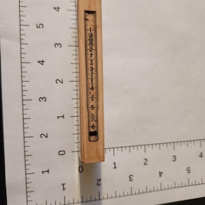 May include: A small, rectangular wooden ruler with black markings and numbers. The ruler is marked with inches and has the text "RIDGID No. 618 Plumbers Rule" printed on it. The ruler is approximately 6 inches long.