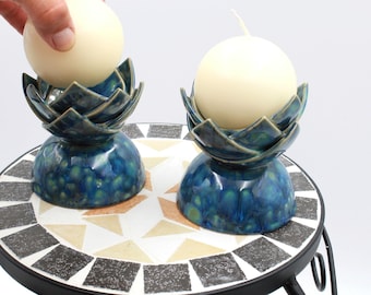 May include: Two blue and green ceramic candle holders with white candles. The candle holders are shaped like pineapples and have a textured finish.